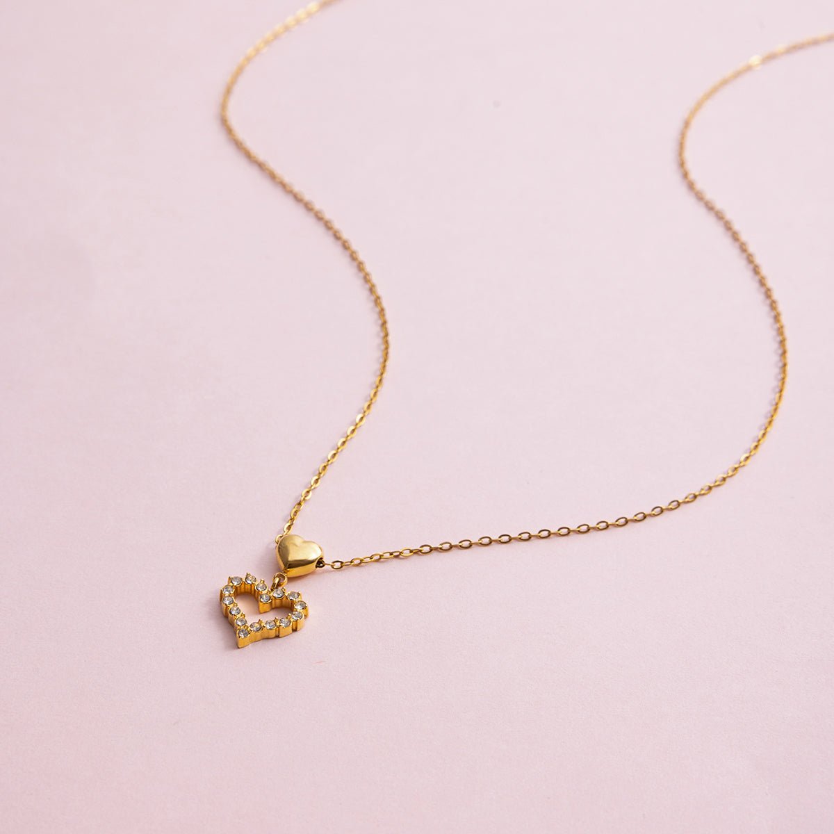 Gold heart-shaped pendant necklace on a pink background