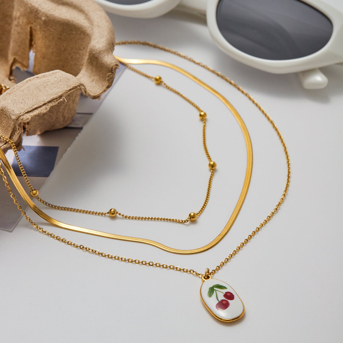 Gold necklace with a cherry pendant on a light surface
