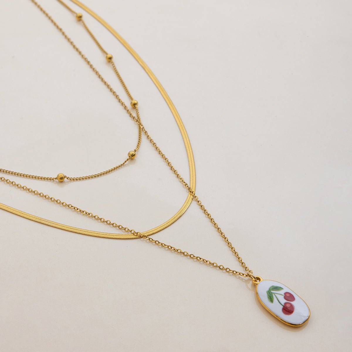 Gold necklaces with a pendant featuring cherries on a beige background