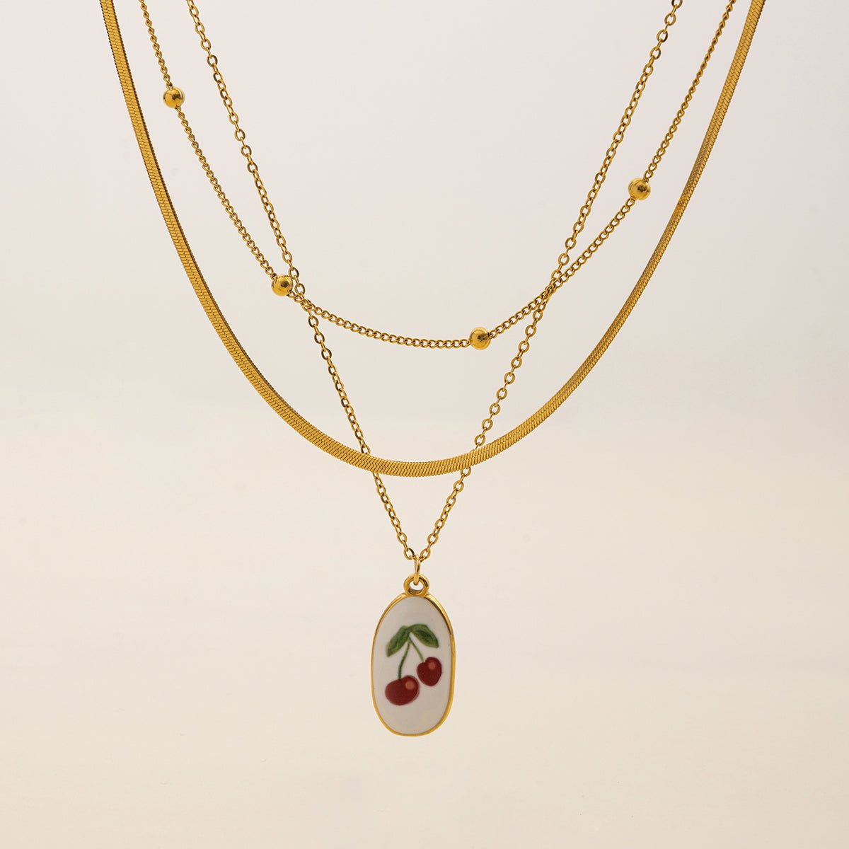 Gold necklace with a cherry pendant on a beige background
