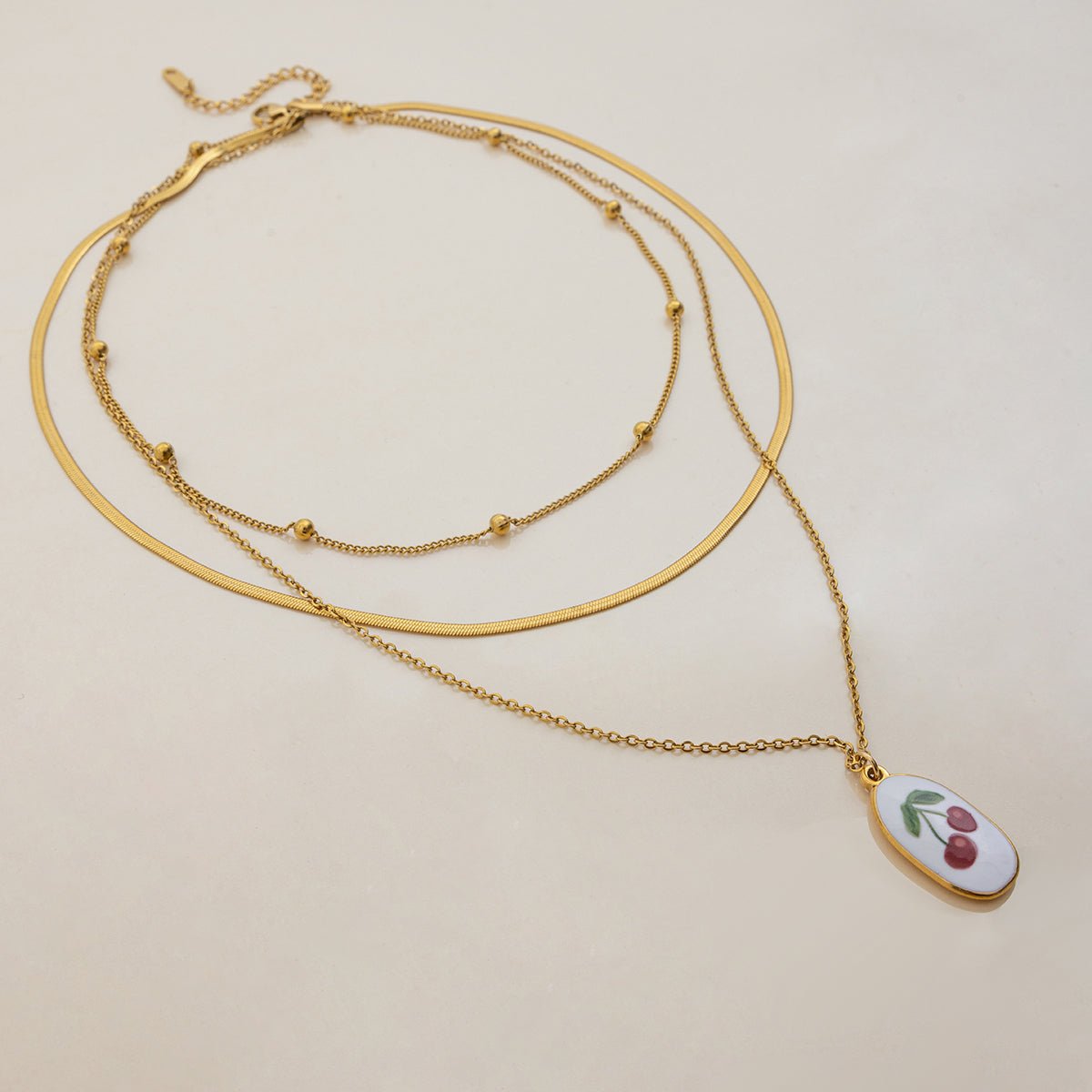 Gold necklace with a cherry pendant on a beige background