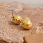 Gold teardrop-shaped earrings on a textured stone surface