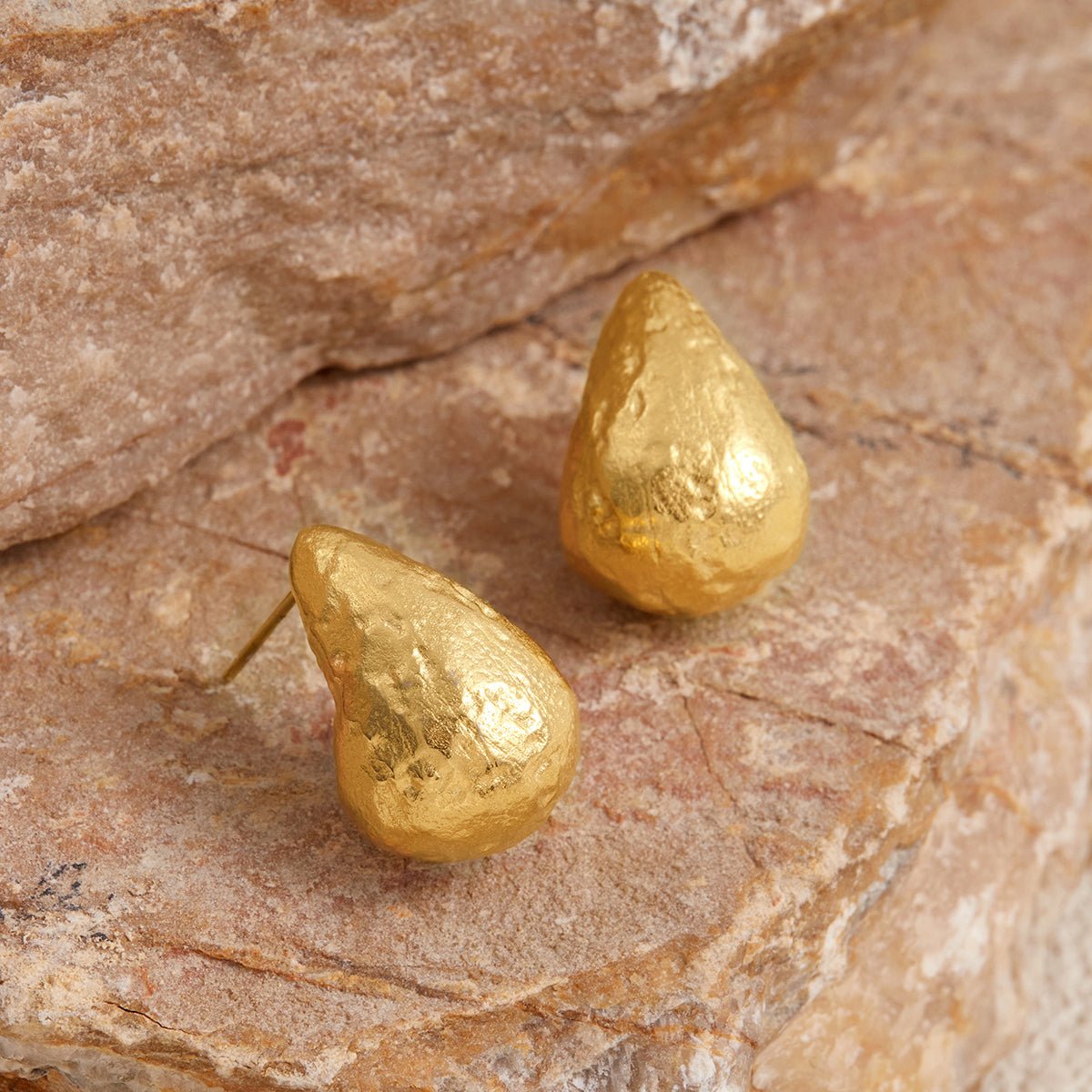 Gold teardrop-shaped earrings on a stone surface