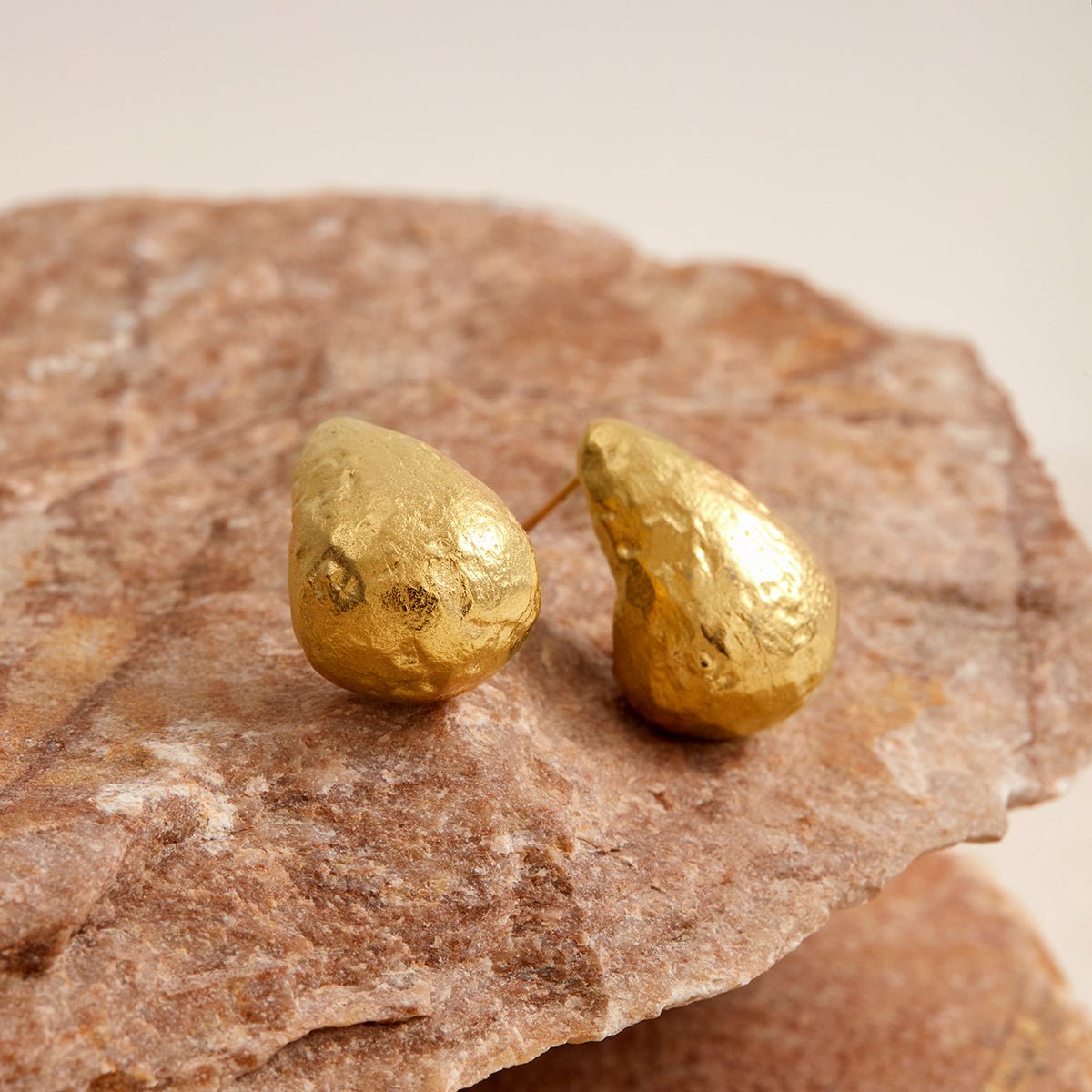Gold teardrop-shaped earrings on a stone surface