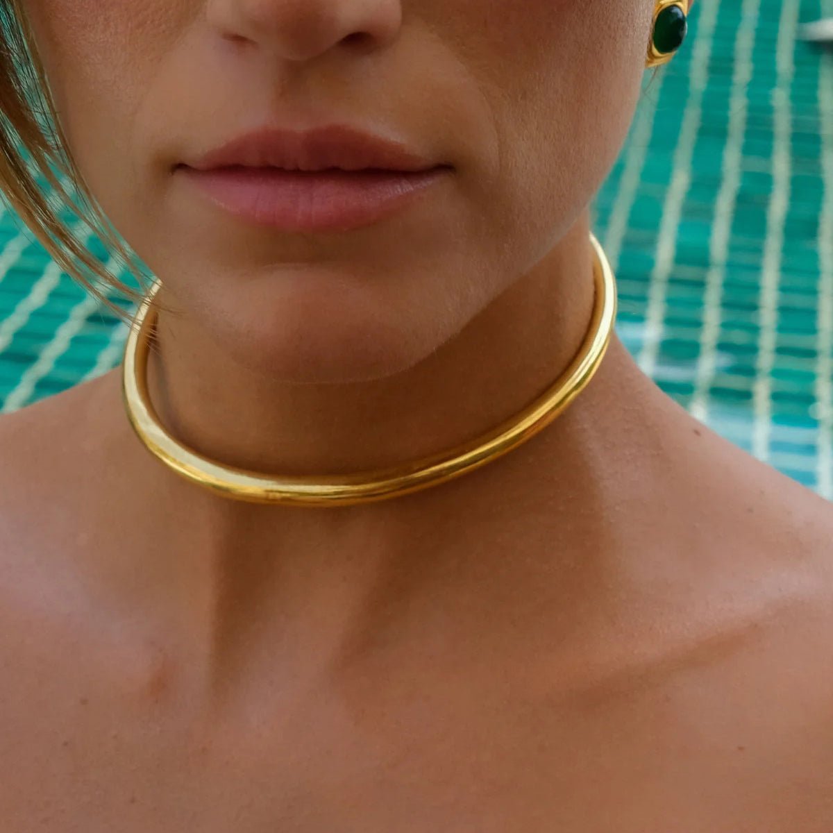 Close-up of a person wearing a gold choker necklace with a blurred background.