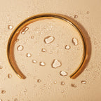 Gold hoop earring with water droplets on a beige background