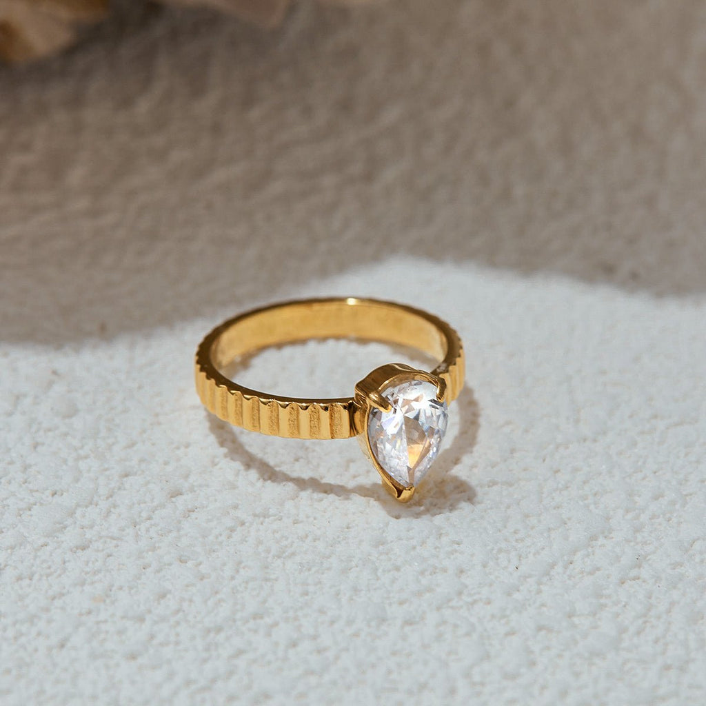Gold ring with a clear teardrop-shaped gemstone on a textured surface