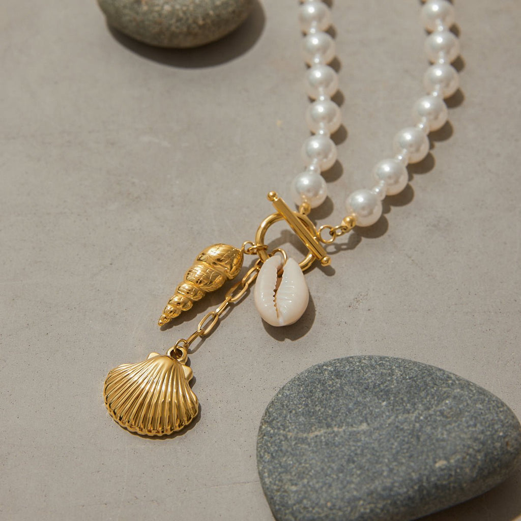 Pearl necklace with gold shell charms on a stone surface