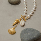 Pearl necklace with gold shell charms on a stone surface