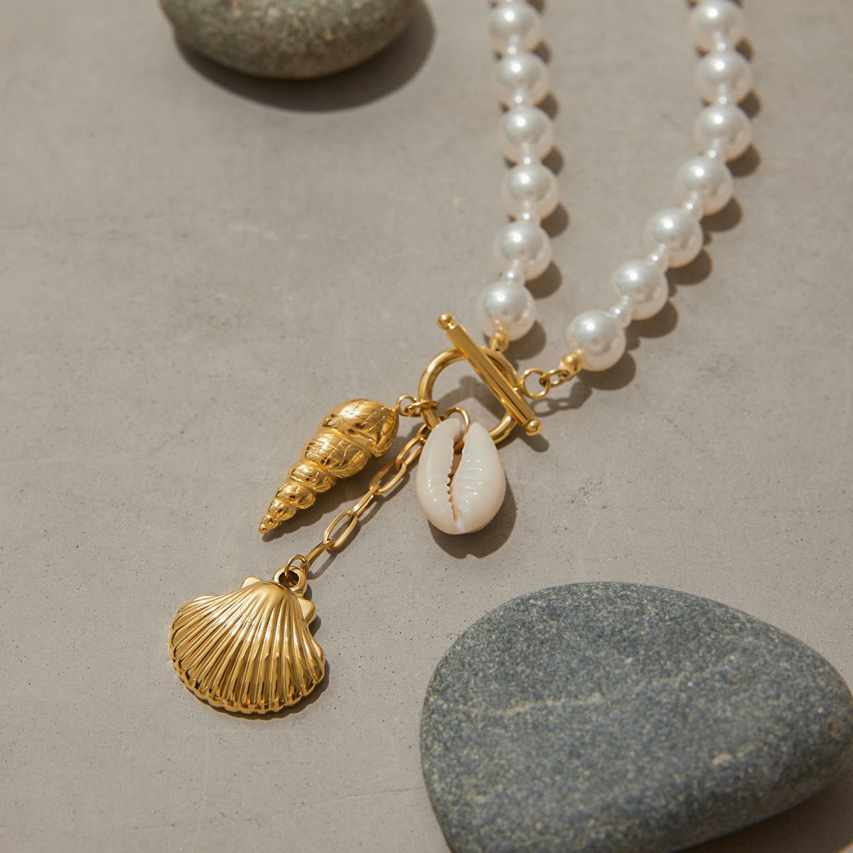 Pearl necklace with gold shell charms on a stone surface