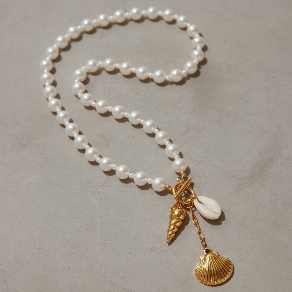 Pearl necklace with gold shell charms on a neutral background