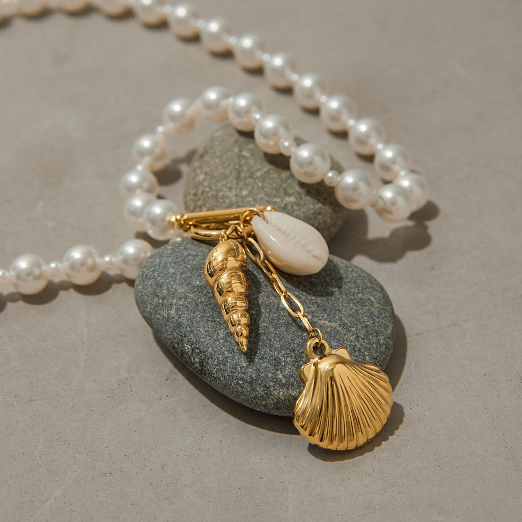 Pearl necklace with gold shell charms on a stone surface