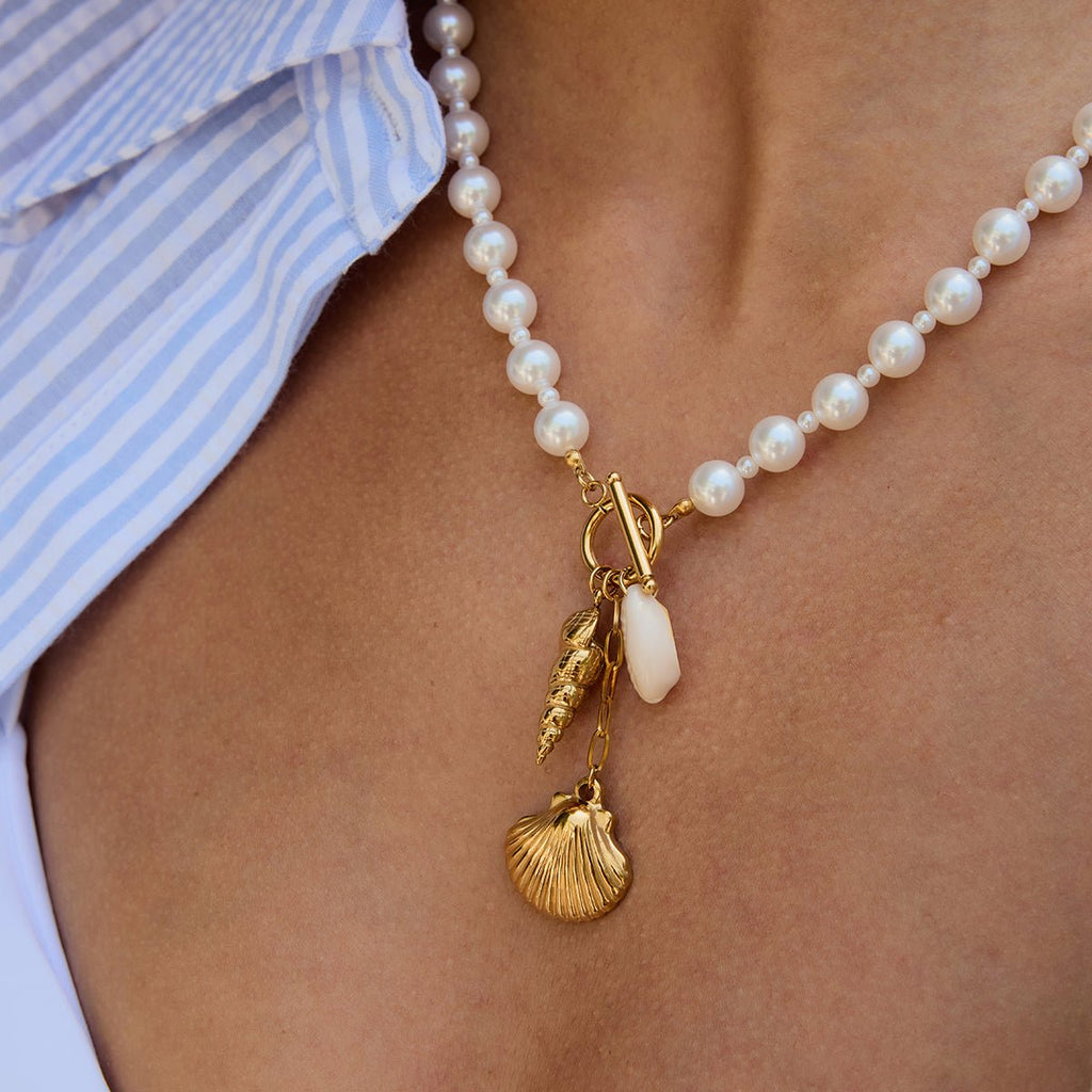 Pearl necklace with gold charms worn by a person