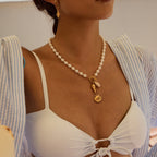 Woman wearing a pearl necklace with a gold pendant, dressed in a white top and striped shirt.
