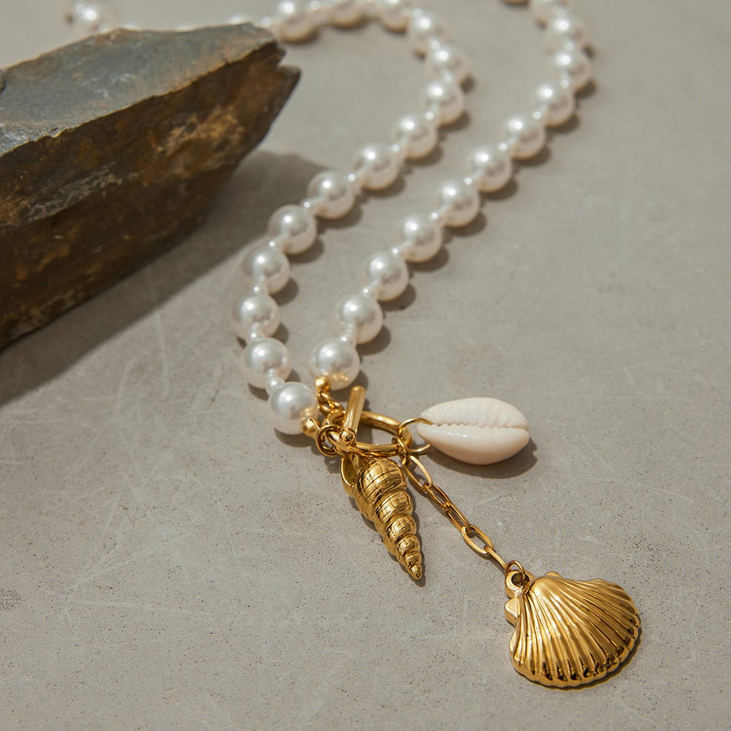 Pearl necklace with gold shell charms on a textured surface