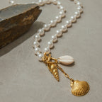 Pearl necklace with gold shell charms on a textured surface