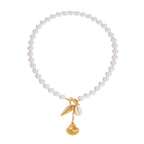 Pearl bracelet with gold charm featuring a leaf and shell on a white background