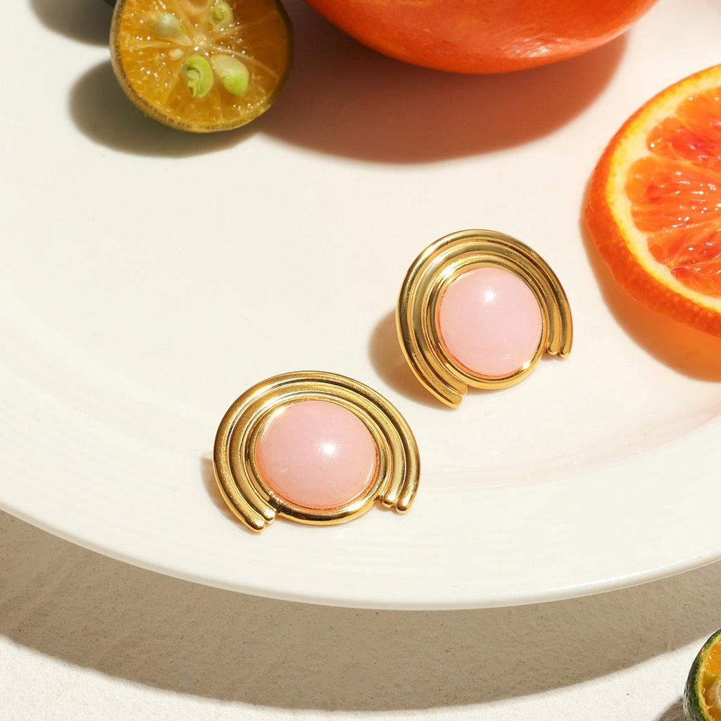 Gold earrings with pink stones on a white plate with sliced fruits