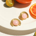 Gold earrings with pink stones on a white plate with sliced fruits