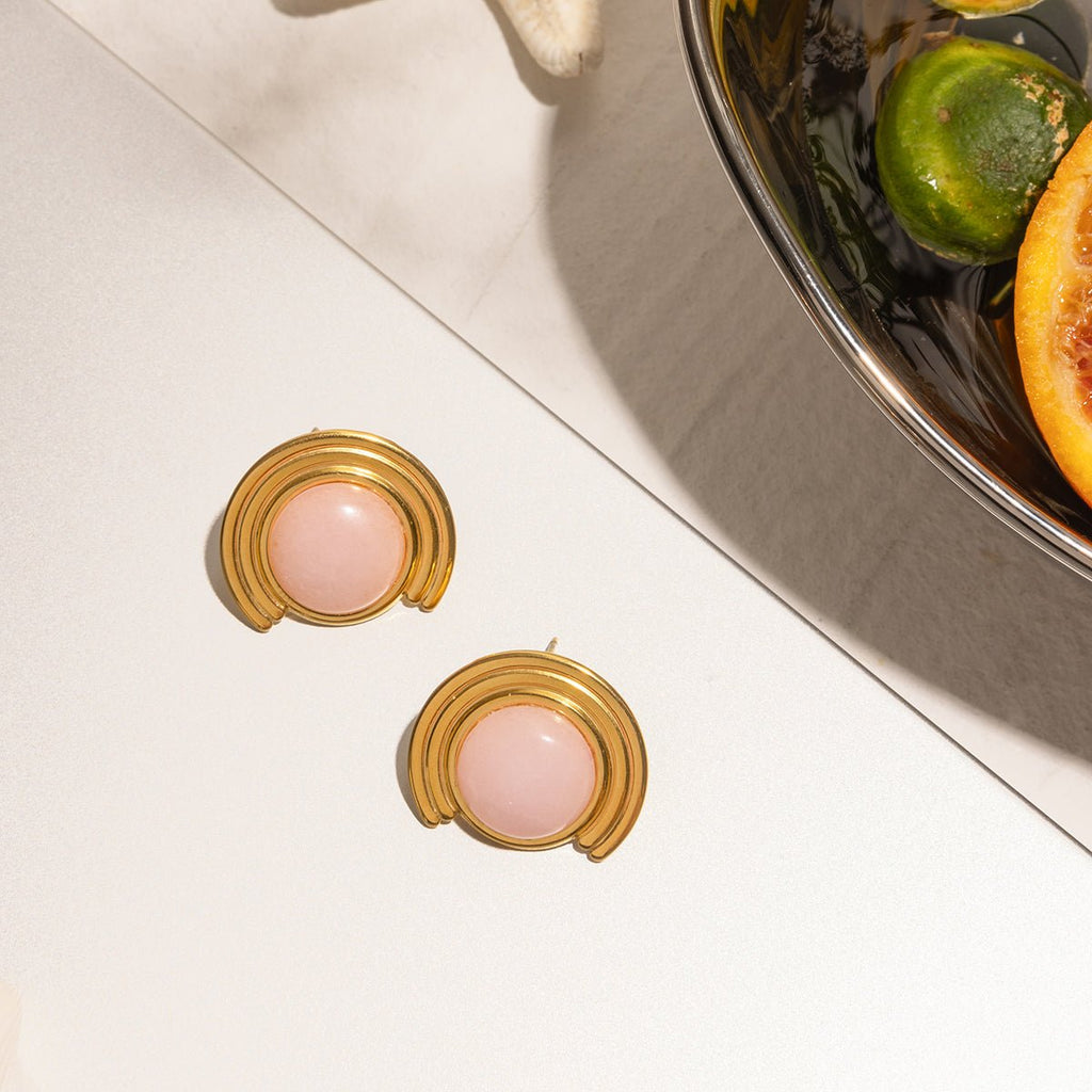 Gold earrings with pink stones on a white surface