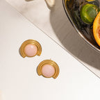 Gold earrings with pink stones on a white surface