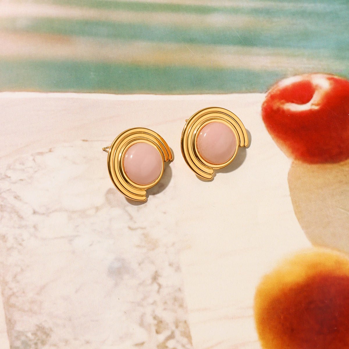 Gold earrings with pink stones on a natural stone surface