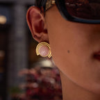 Close-up of an ear wearing a gold earring with a pink gemstone, blurred background