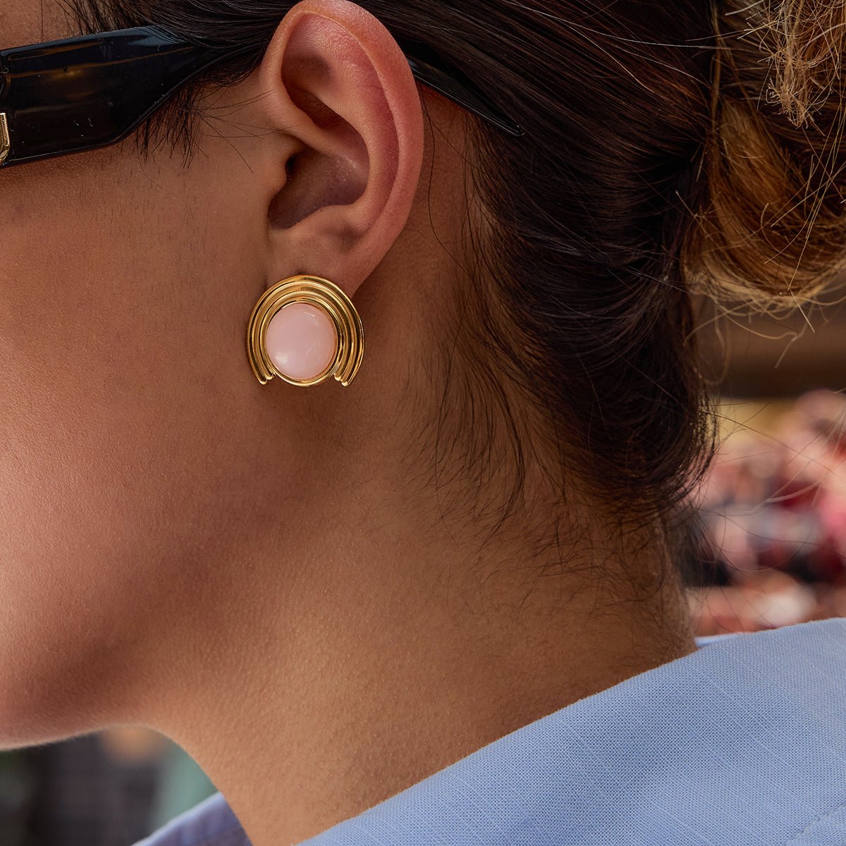 Close-up of a person wearing a gold earring with a pink gemstone.