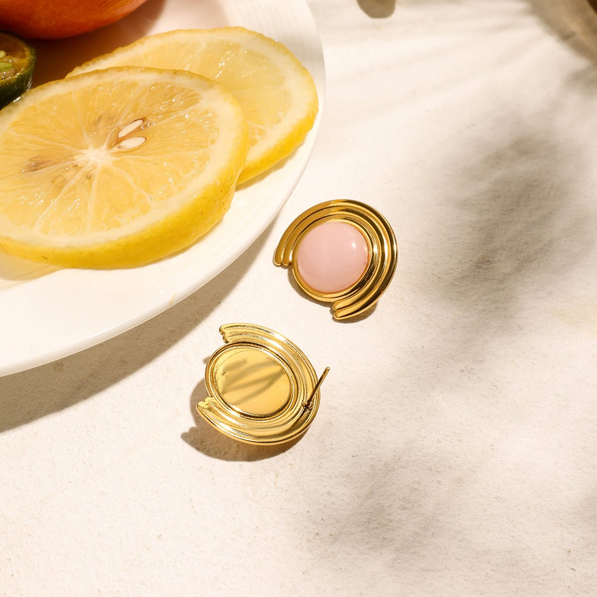 Two gold compacts with pink cream on a white surface with lemon slices in the background.