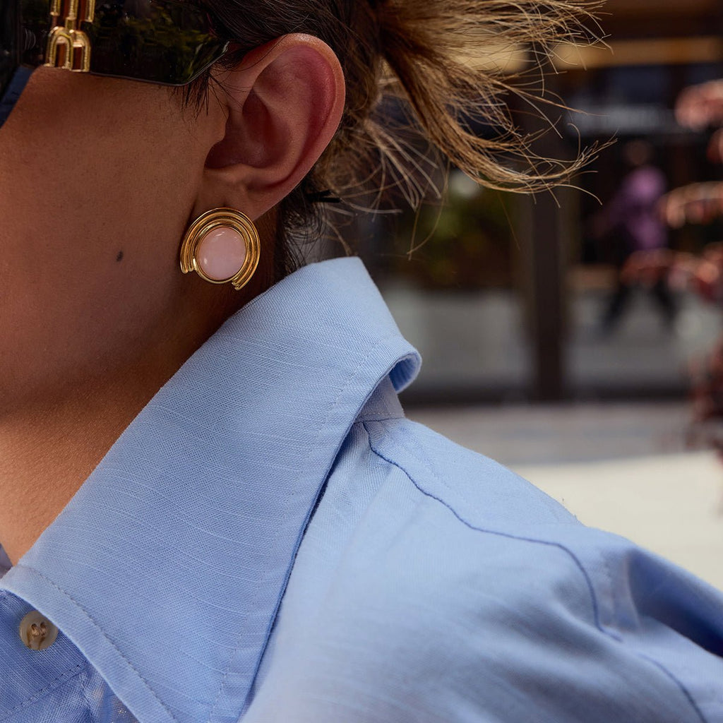 Close-up of a person wearing a gold earring with a pink gemstone, blurred background
