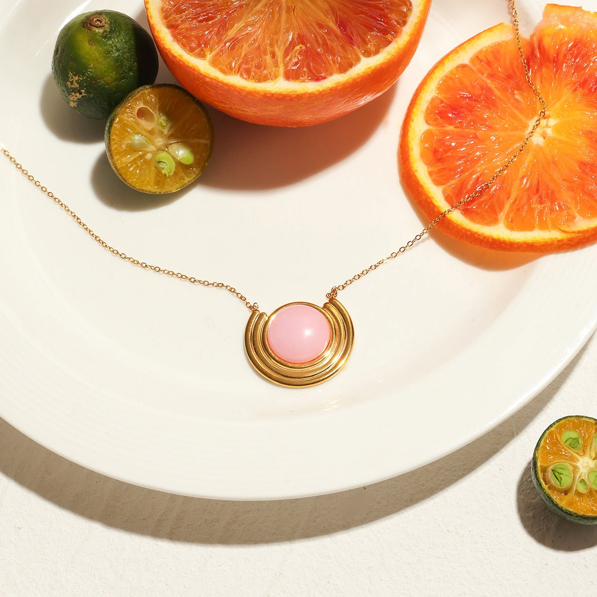 Necklace with pink pendant on a white surface with sliced oranges and limes.