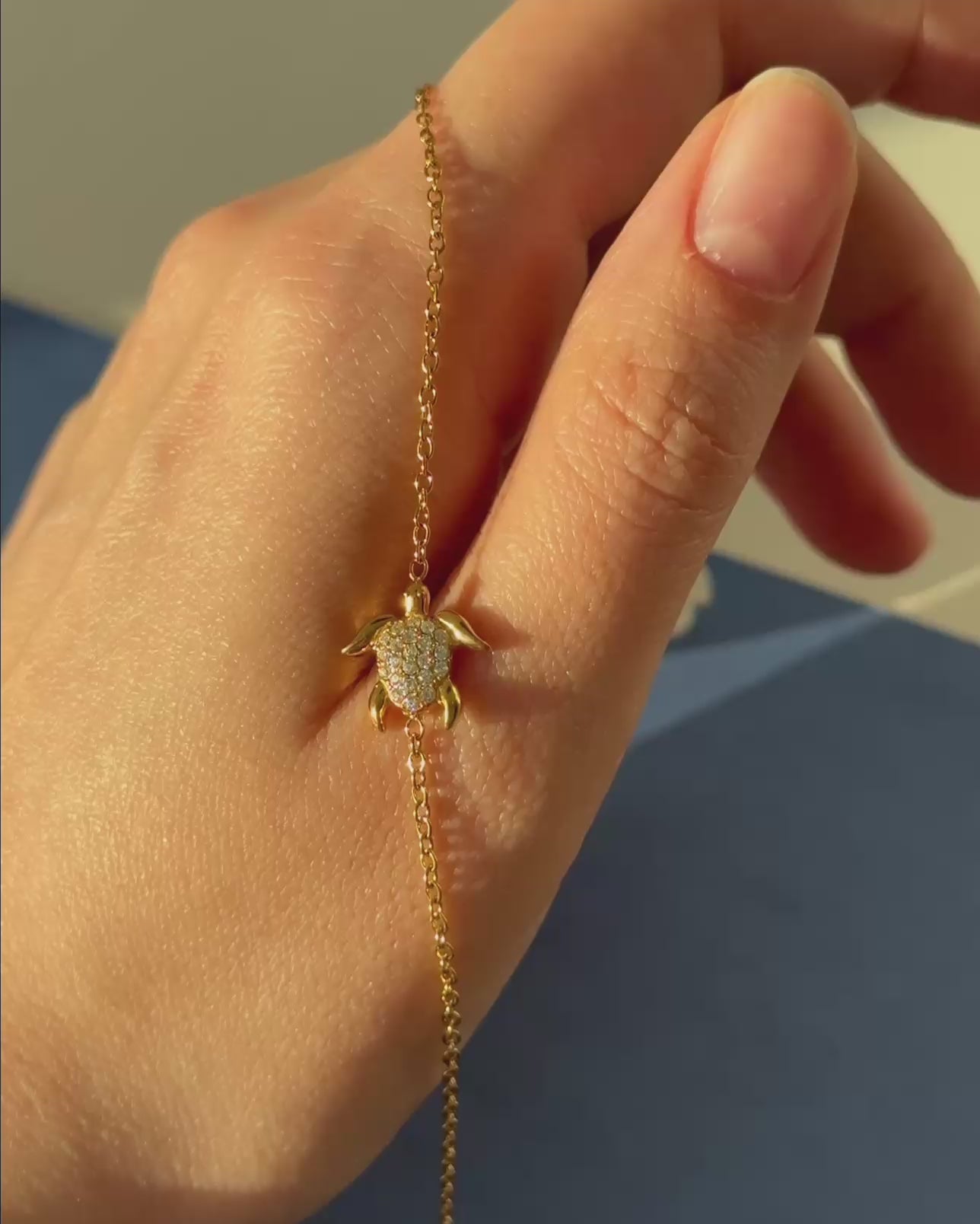 Close-up of a gold turtle bracelet held in the sunlight, reflecting a bright, brilliant gleam off its polished surface.