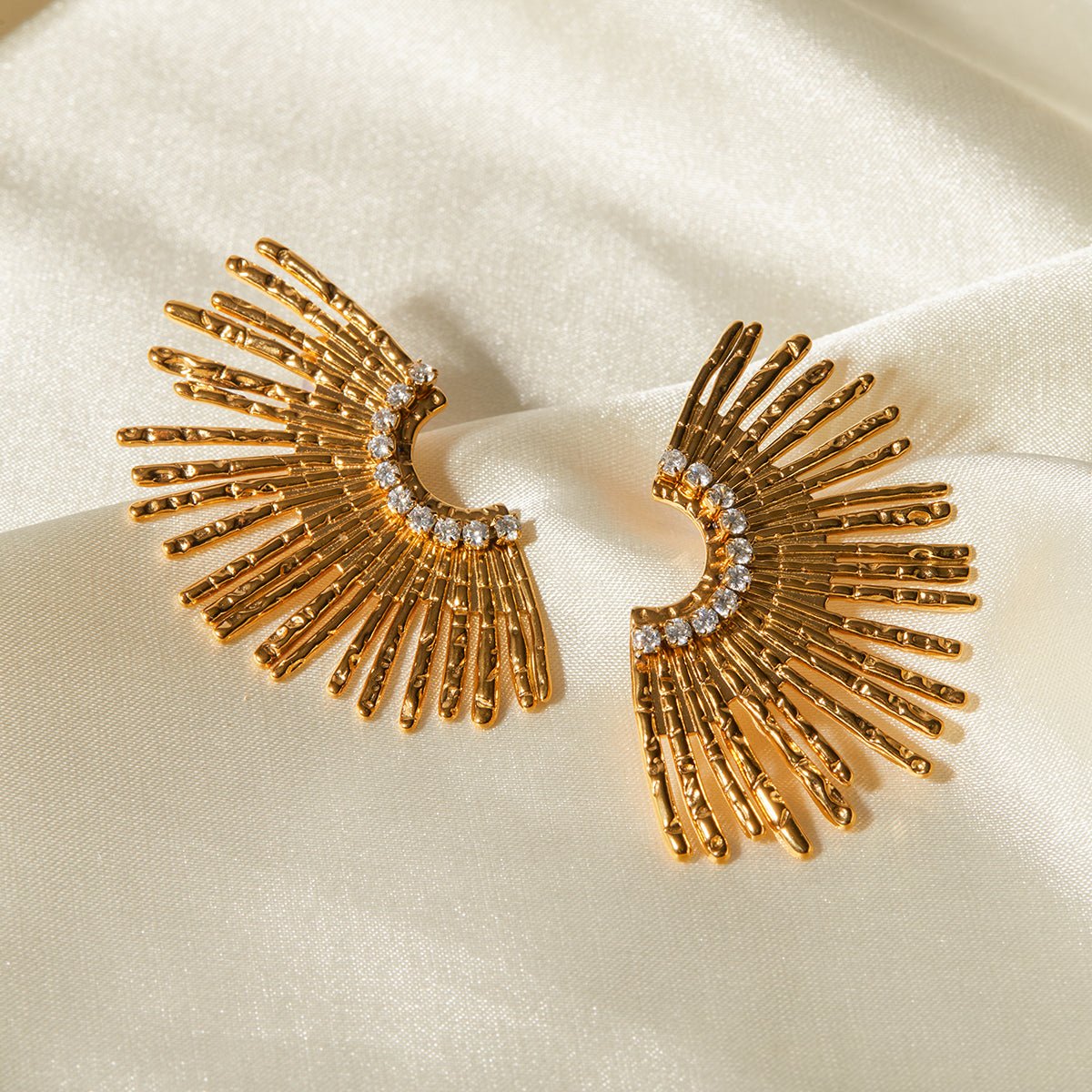 Gold earrings with fan-like design on a beige fabric background