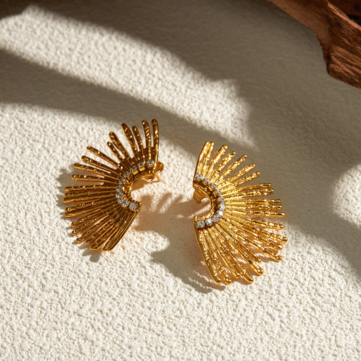 Gold earrings with fan-like design on a textured beige surface
