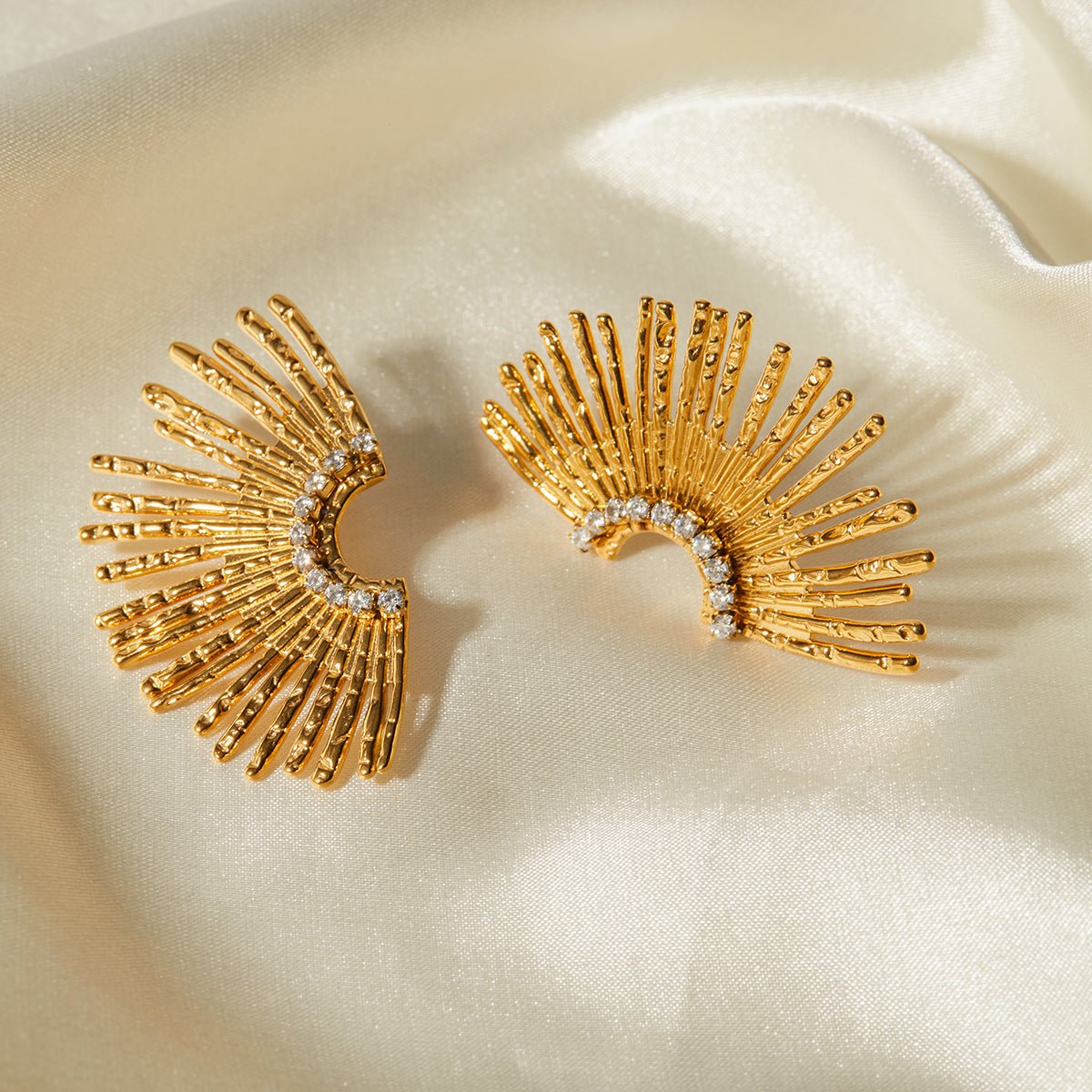 Gold earrings with fan-like design on a beige fabric background