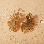 Gold earrings with fan-like design on a textured gold background