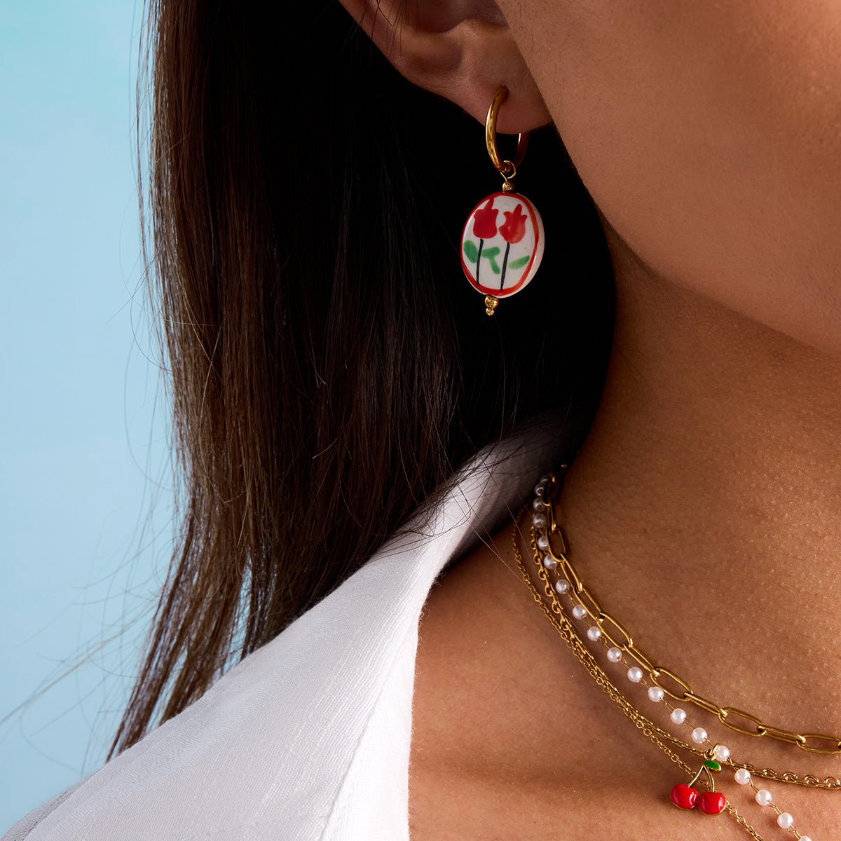 Close-up of a person wearing a floral earring and pearl necklace against a light blue background