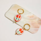 Pair of earrings with red floral design on a light pink stone background