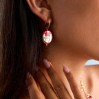Close-up of a woman wearing a red and white earring with a gold setting.