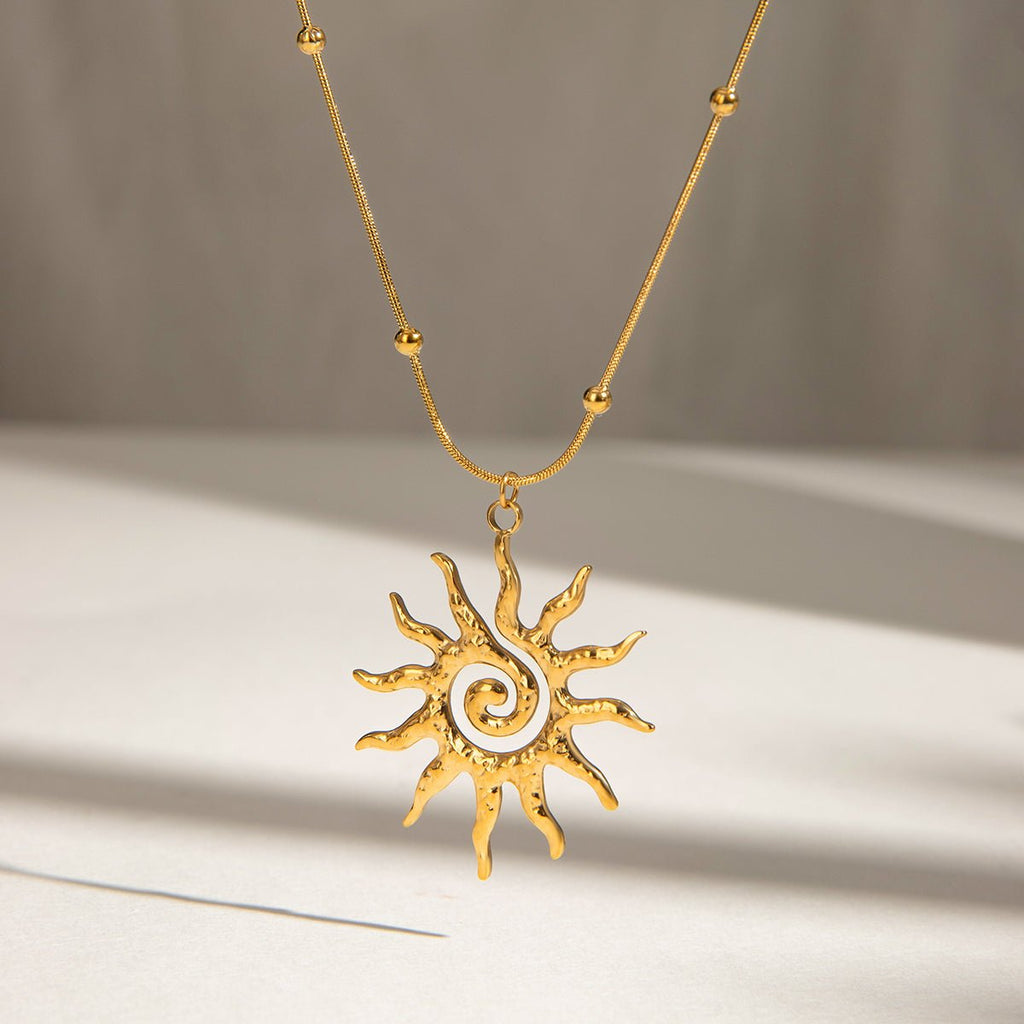 Gold sun-shaped pendant necklace on a neutral background