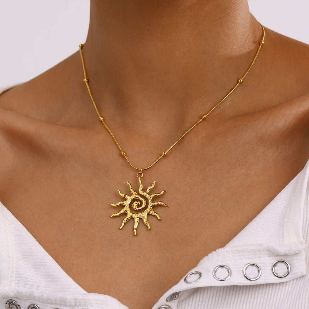 Gold sun-shaped necklace on a person wearing a white top with silver embellishments.