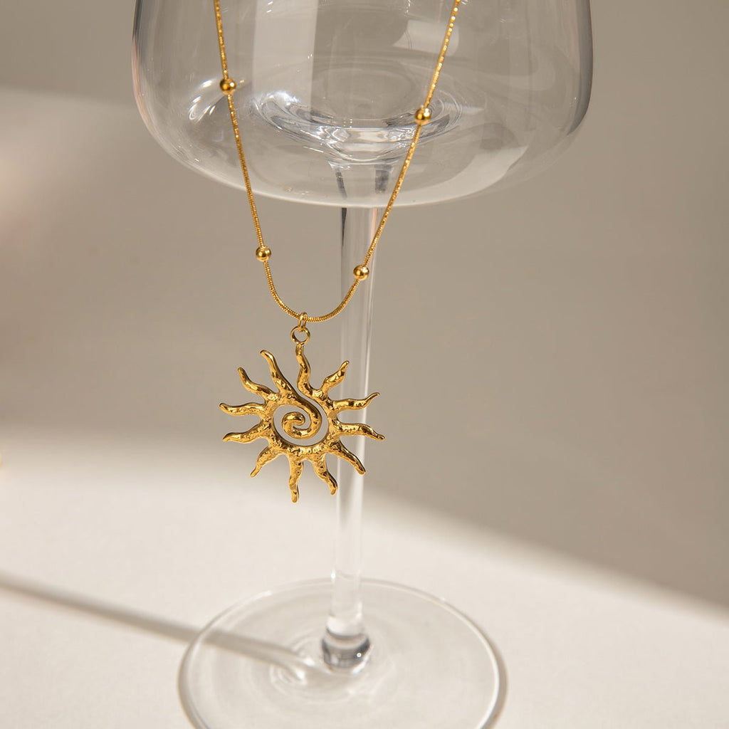 Gold sun-shaped wine glass charm hanging from a clear glass.