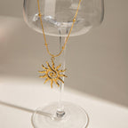Gold sun-shaped wine glass charm hanging from a clear glass.
