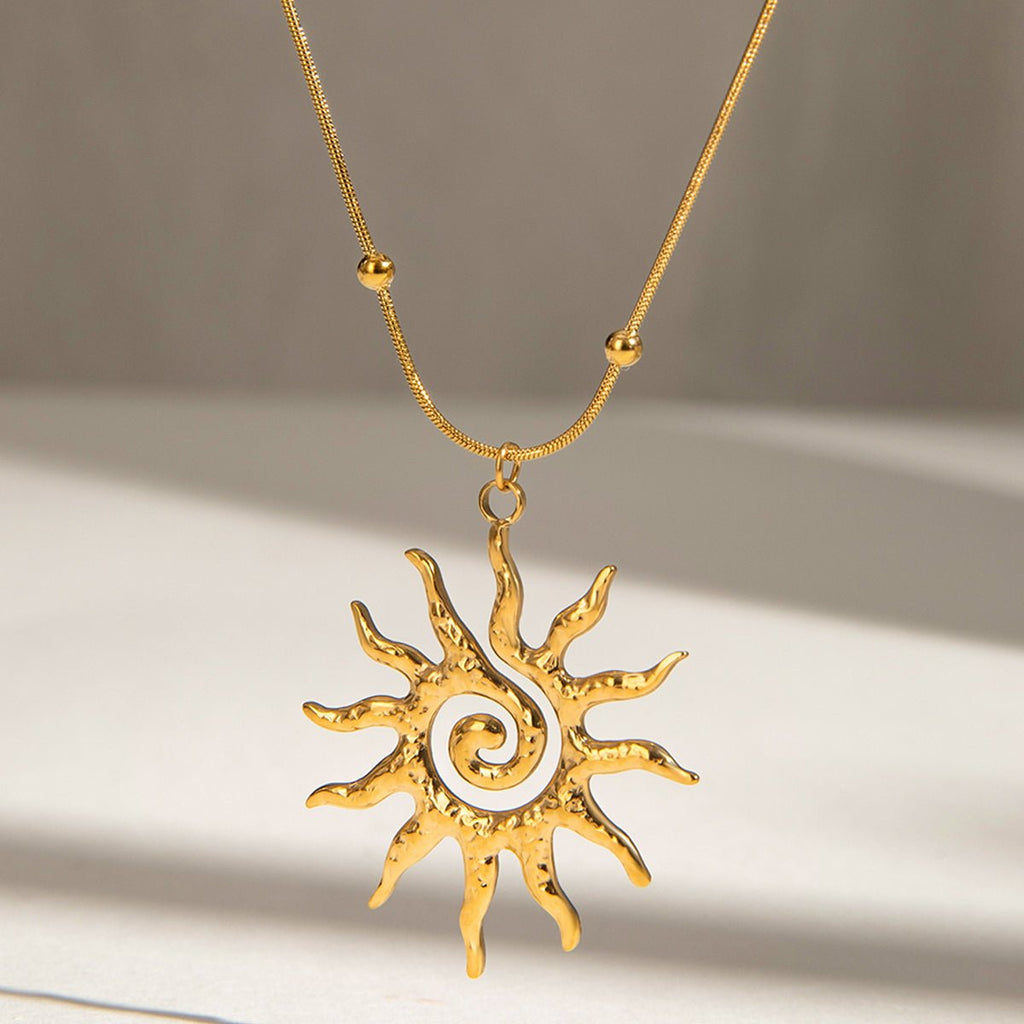 Gold sun-shaped pendant necklace on a neutral background