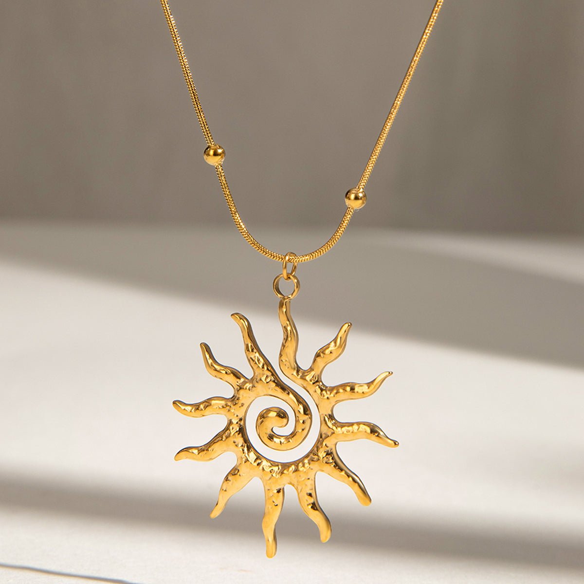 Gold sun-shaped pendant necklace on a neutral background