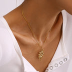 Gold necklace with a sun pendant worn by a person in a white top.