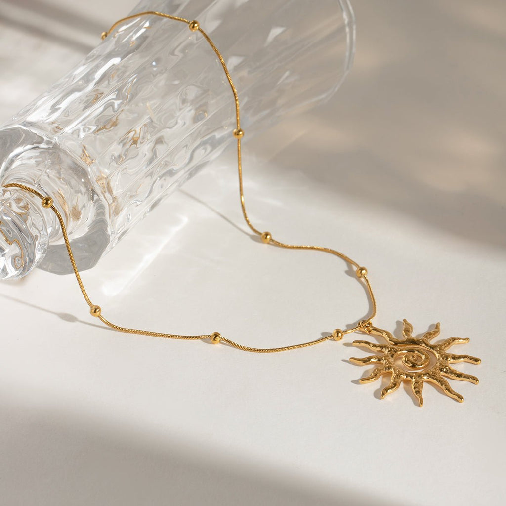 Gold necklace with a sun pendant on a light background