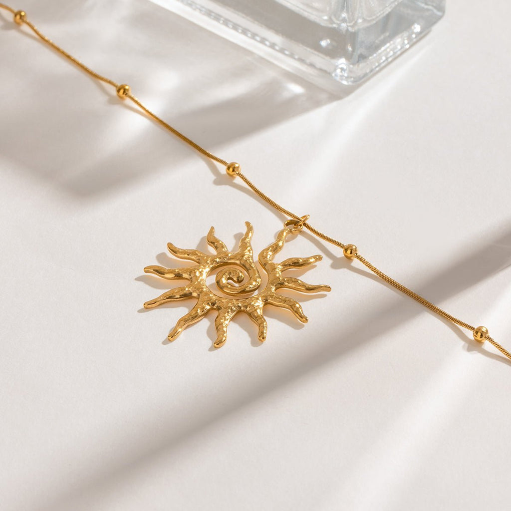 Gold sun-shaped pendant on a gold chain against a white background