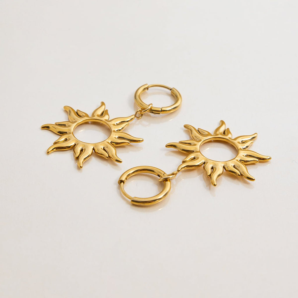 Gold sun-shaped earrings on a light gray background