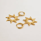 Gold sun-shaped earrings on a light gray background